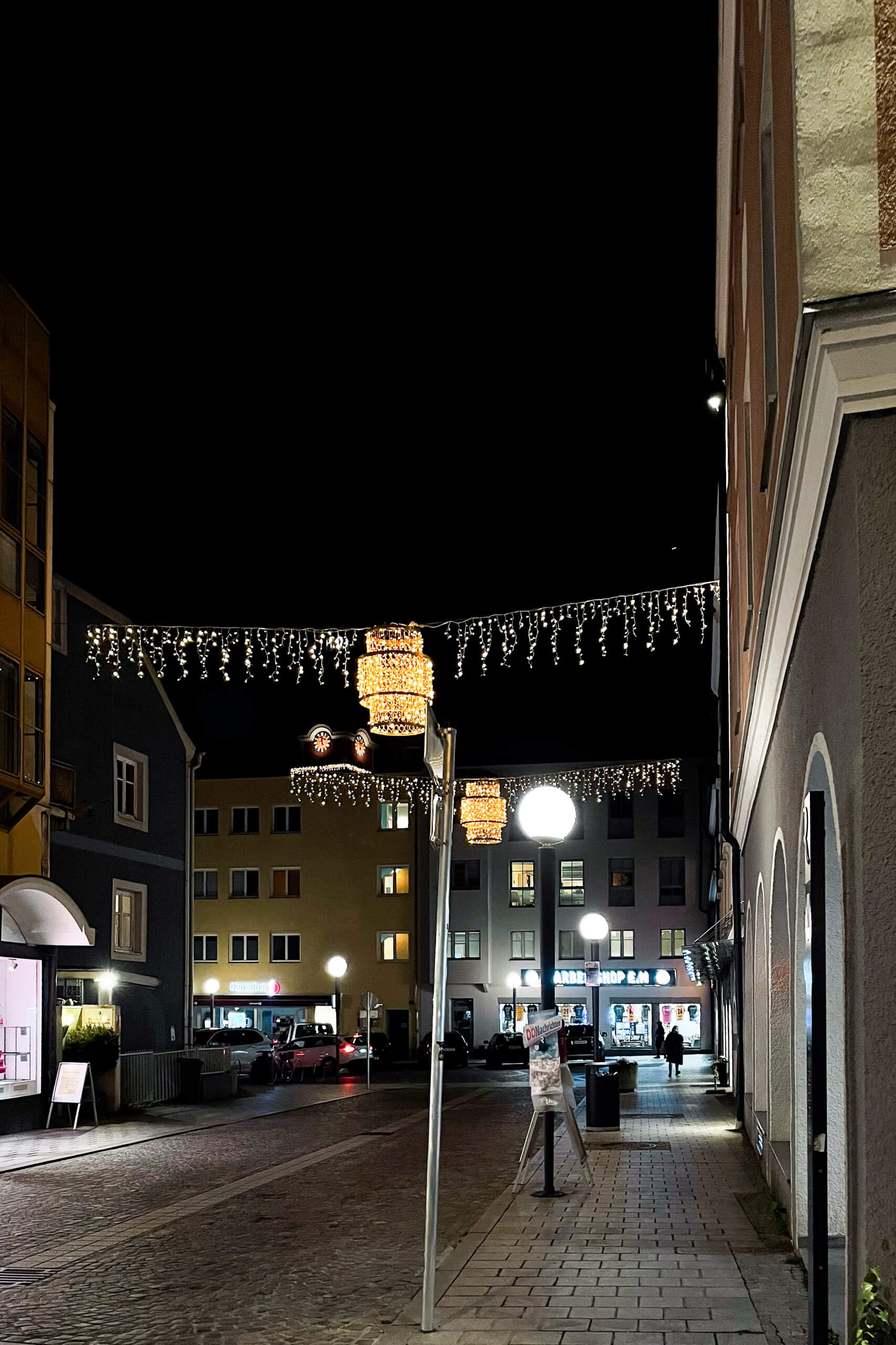 Beleuchtete Einkaufsstraße in der Nacht mit Lichterketten und Schaufenstern.