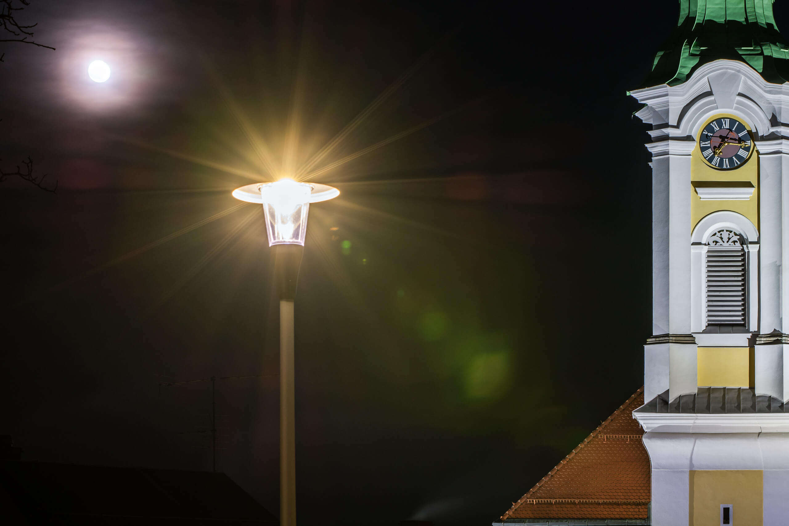 Kirchturm mit Uhr und Straßenlaterne bei Nacht, Mondschein und Linsenreflexionen