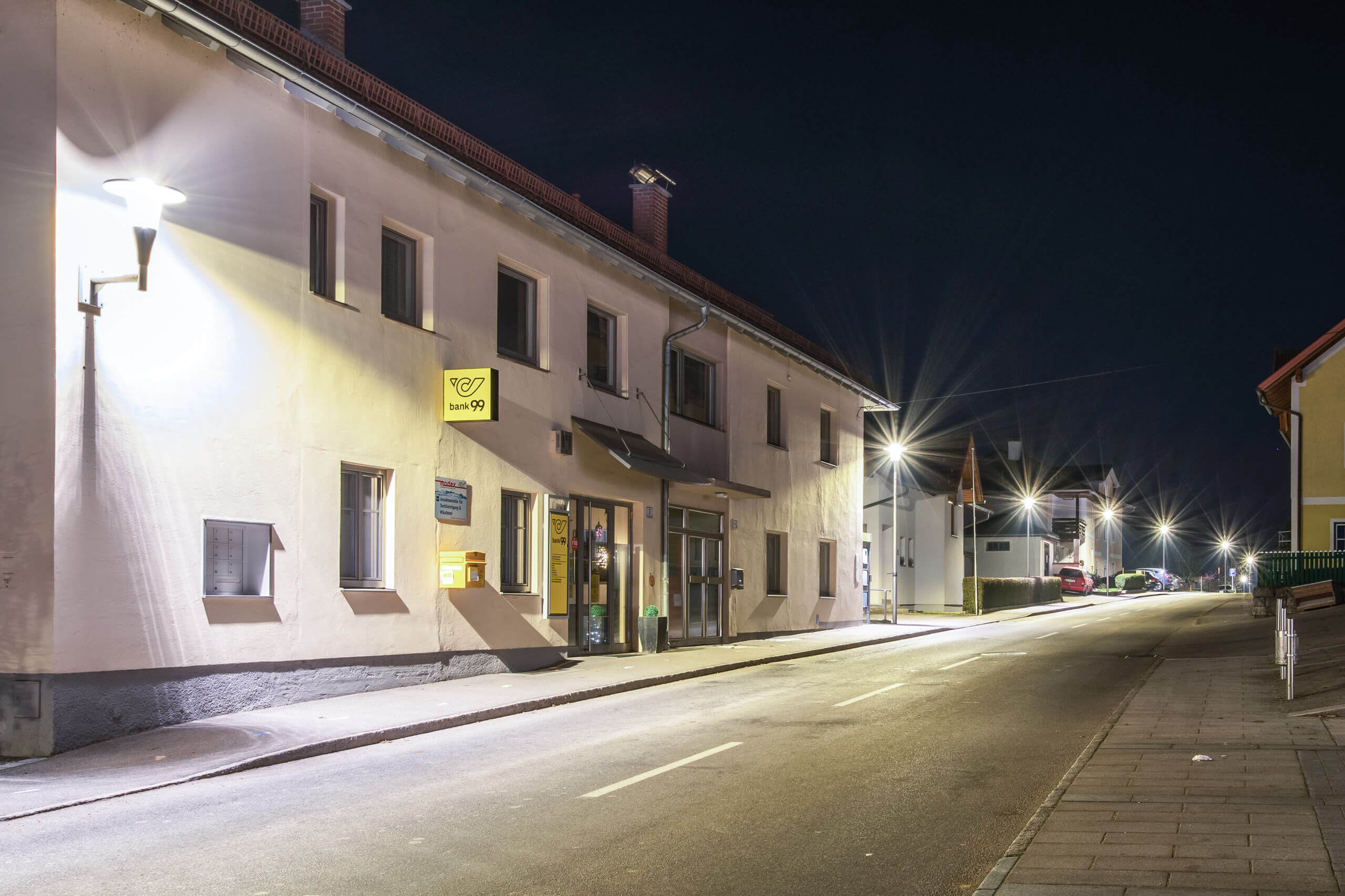 Straßenbeleuchtung und beleuchtetes Gebäude mit "banco99" Logo bei Nacht