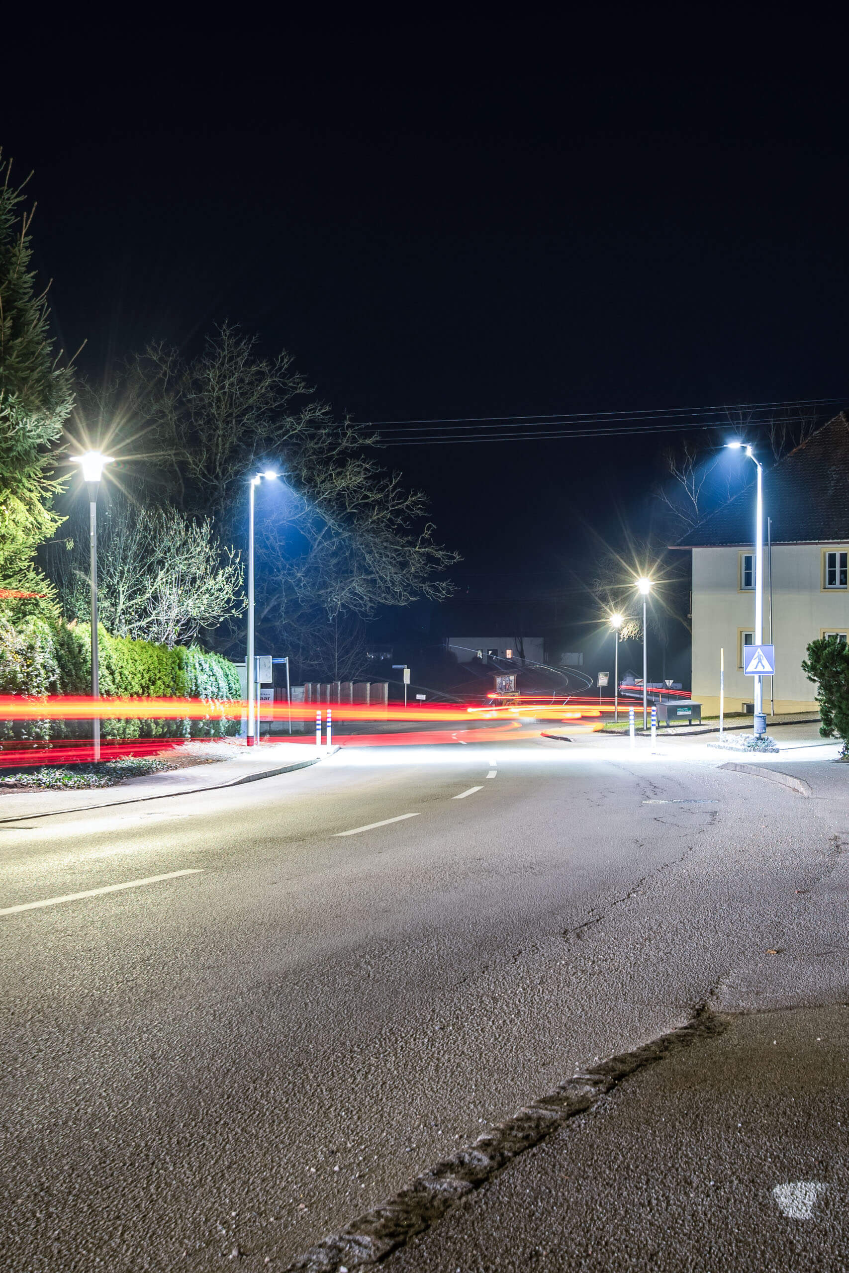 Beleuchtete Straße bei Nacht mit Lichtspuren von fahrenden Autos, Straßenlaternen und Hausbeleuchtung
