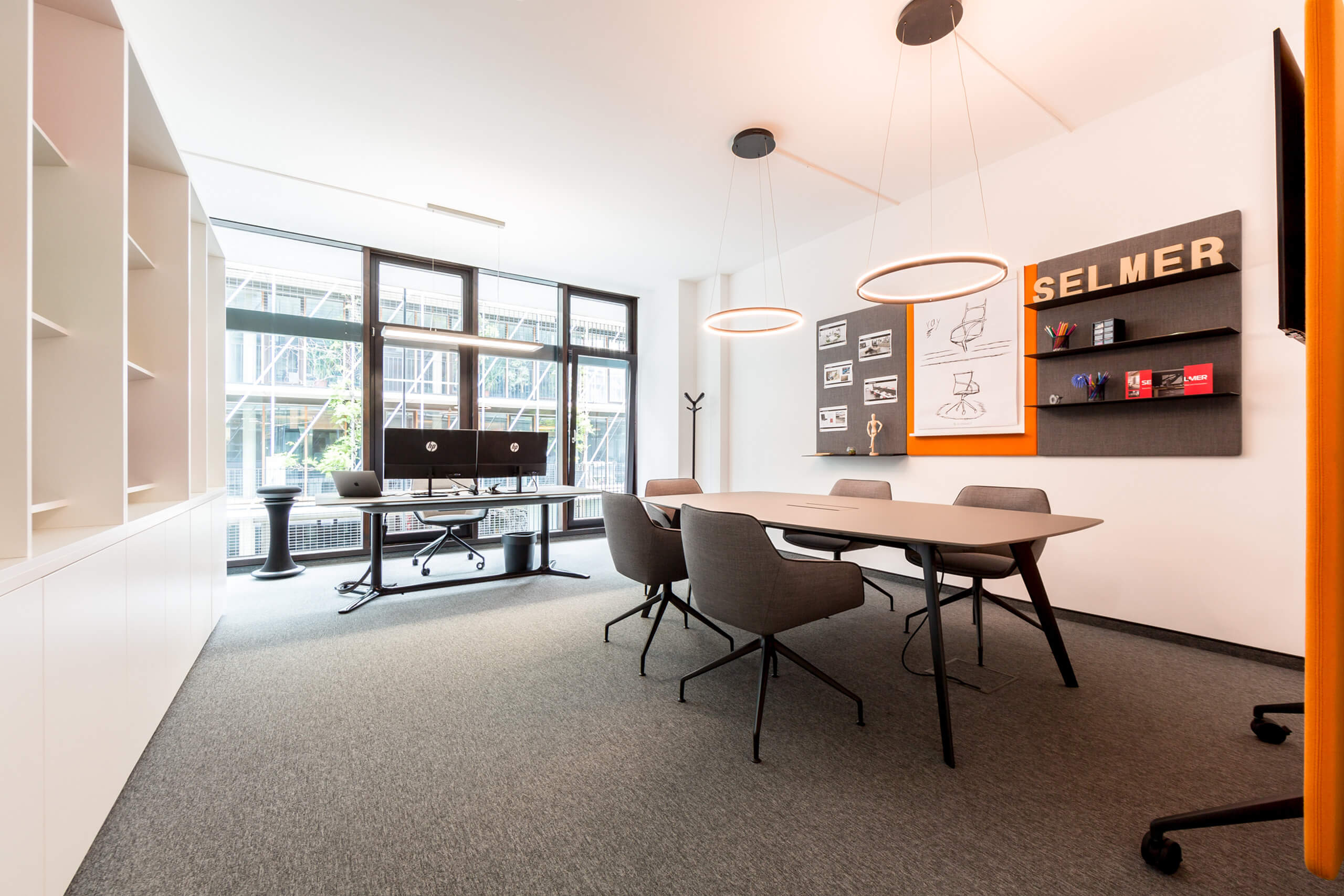 Modernes Büro mit Besprechungstisch und Schreibtisch, beleuchtet durch Ring-Hängeleuchten.