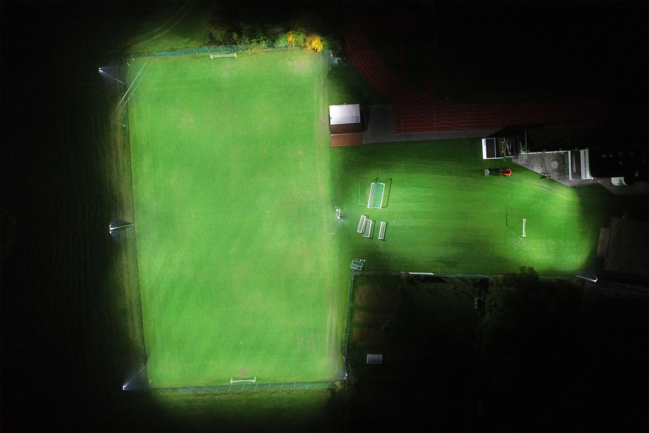 Illumina: Nachtaufnahme eines beleuchteten Fußballplatzes mit Laufbahn und Gebäuden.