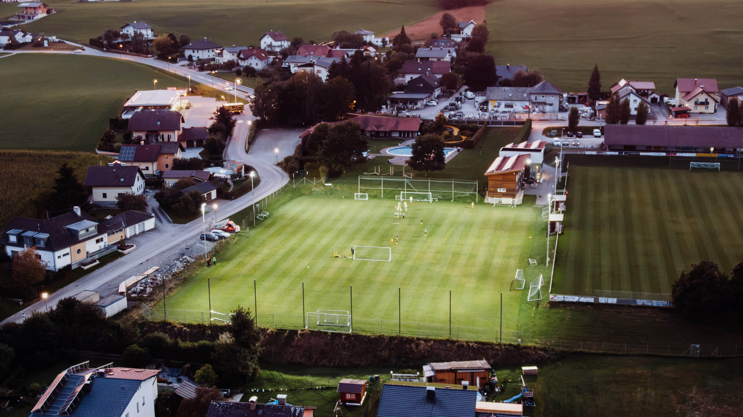 Gefluteter Sportplatz bei Dämmerung mit Fußballspielern – Sportplatzbeleuchtung von Illumina.