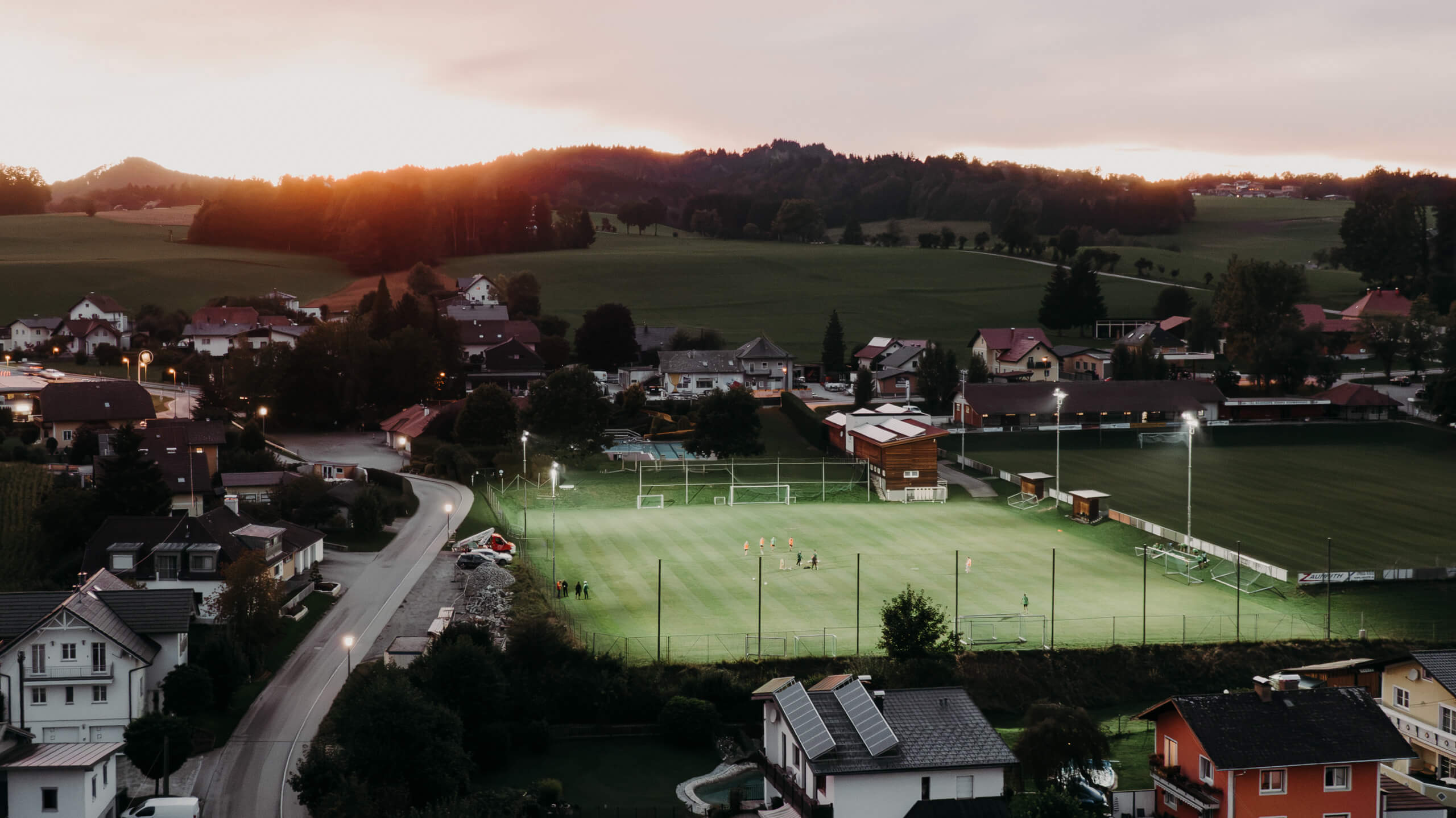 Sportplatzbeleuchtung bei Sonnenuntergang mit Spielern auf dem Feld