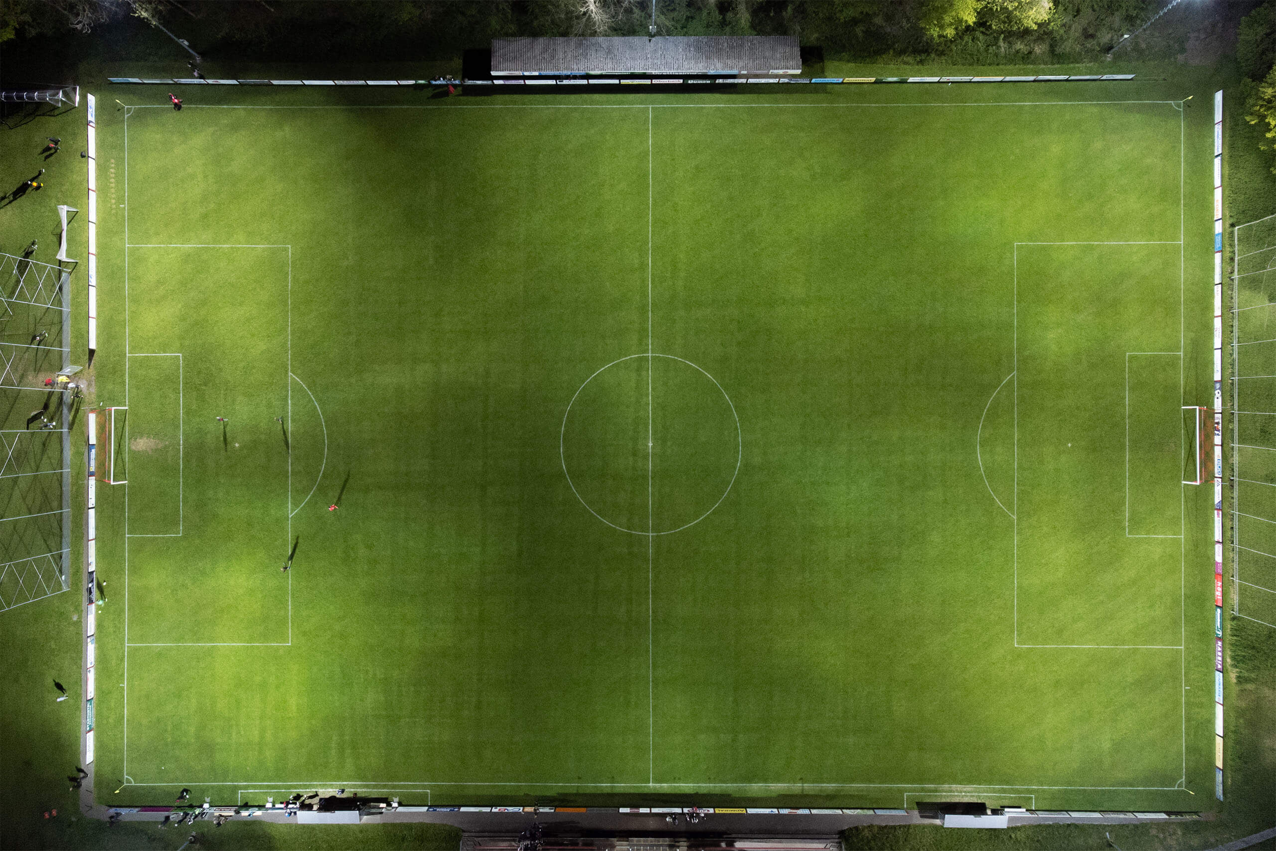 Beleuchteter Fußballplatz bei Nacht mit Spielfeldmarkierungen und Toren.