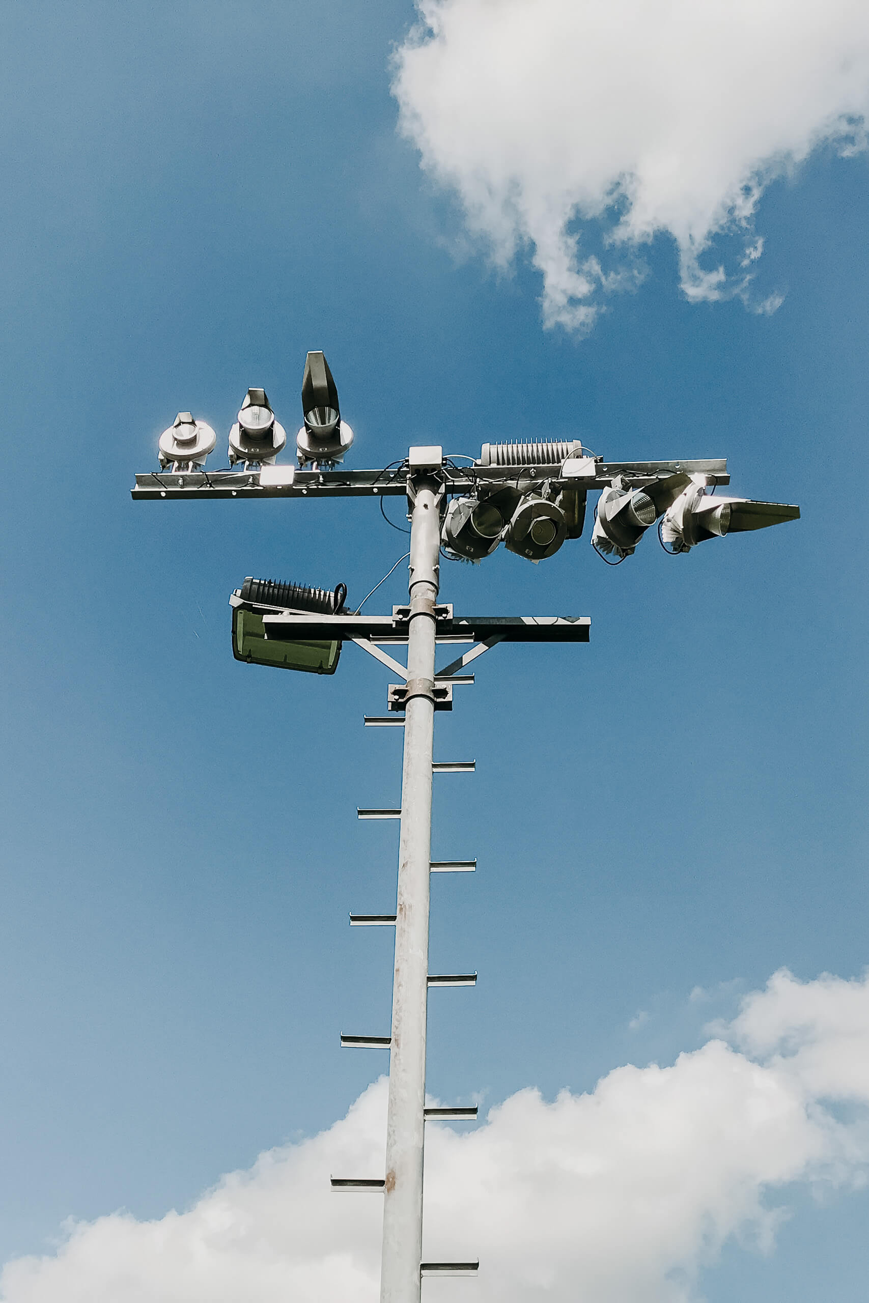 Sportplatzbeleuchtung: Ein Mast mit mehreren Scheinwerfern unter blauem Himmel