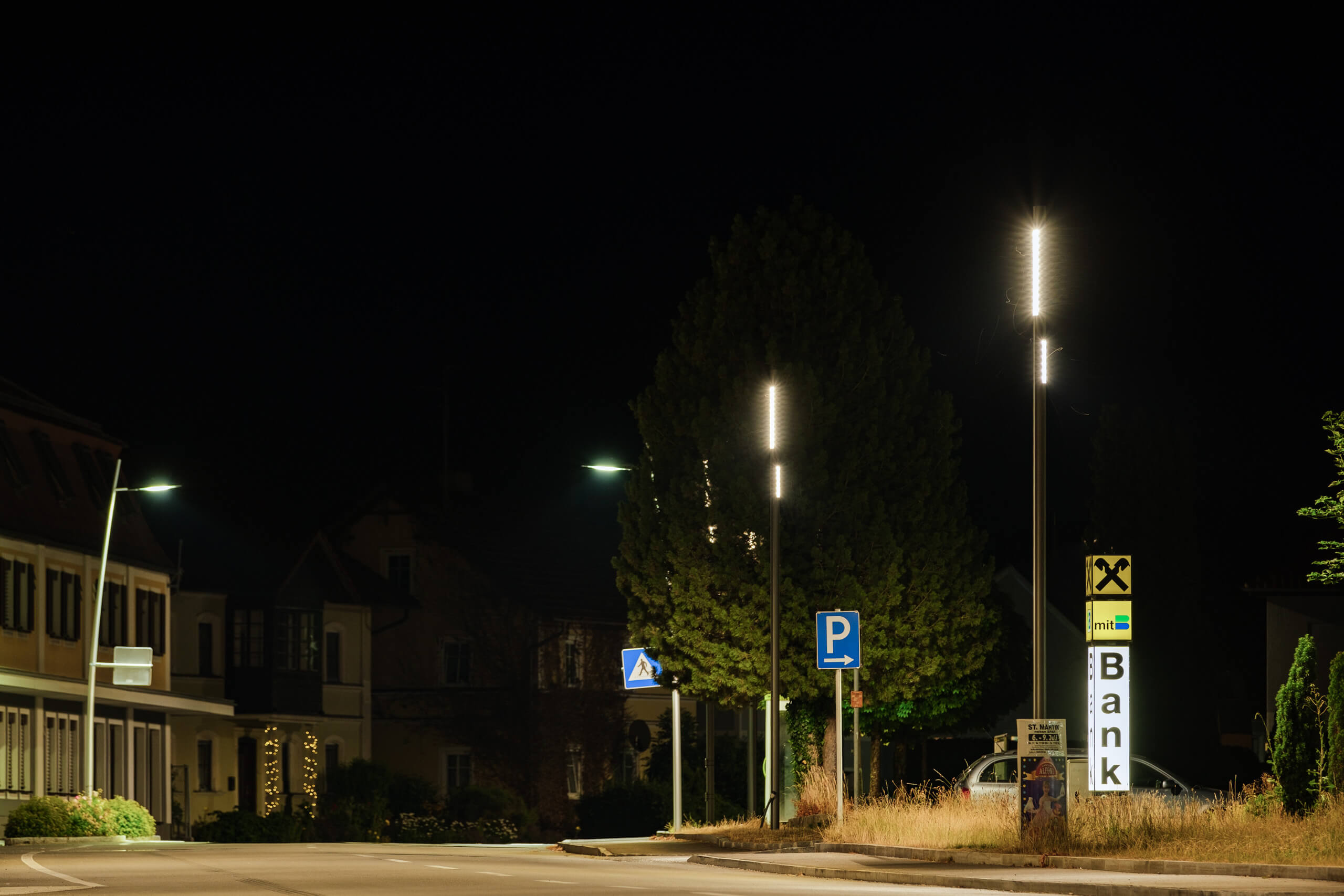 Straßenbeleuchtung mit modernen Leuchten und Bankwerbung in der Nacht.