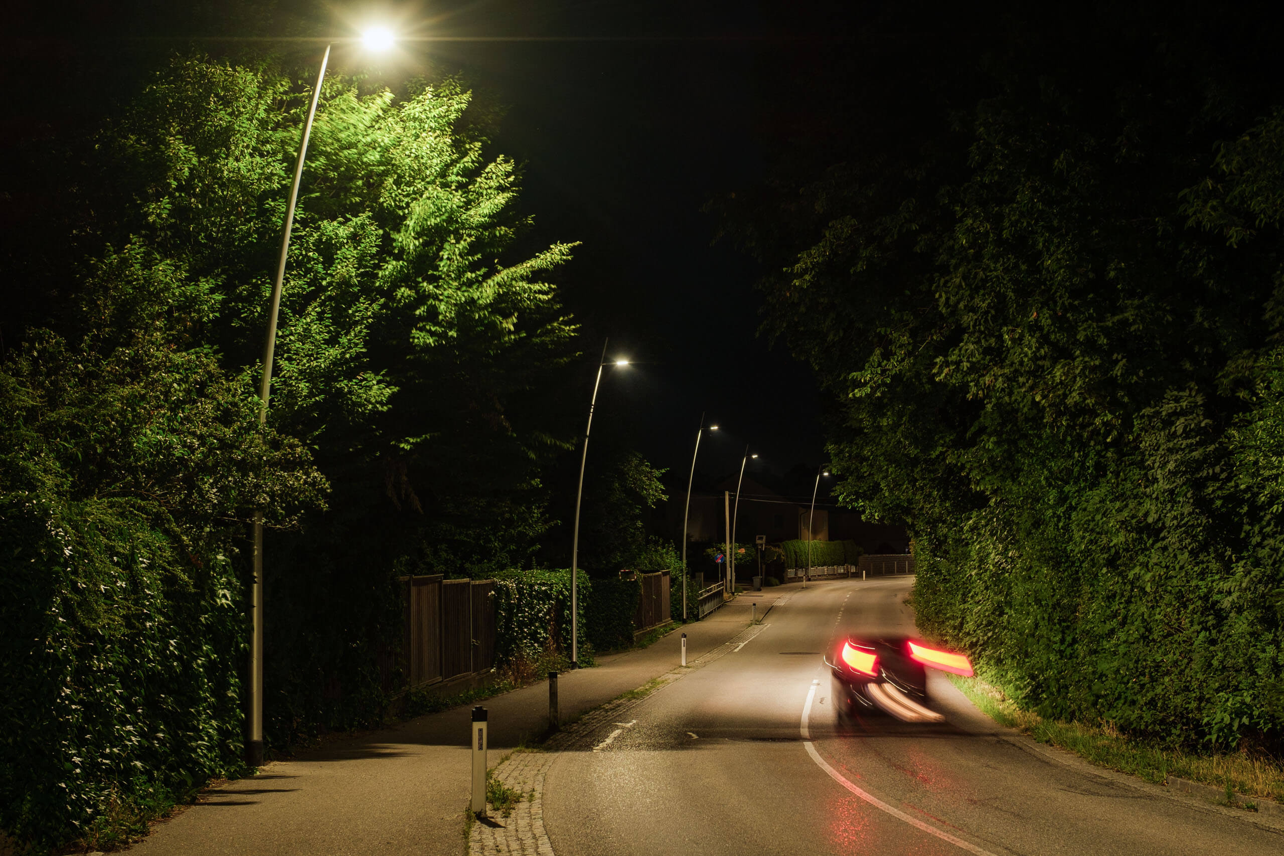 Straßenbeleuchtung von Illumina erhellt nächtliche Allee mit fahrendem Auto