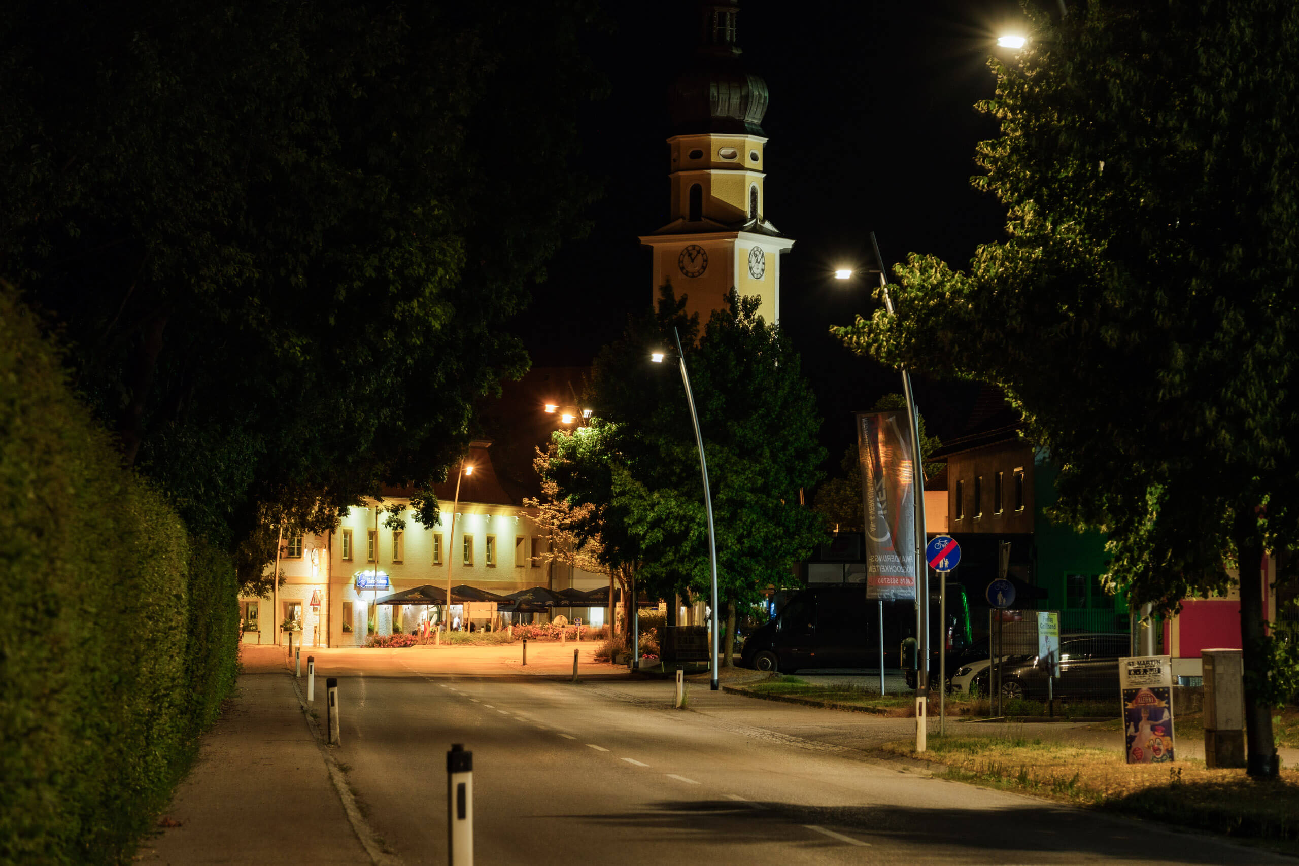 Nachtaufnahme einer beleuchteten Straße mit Kirche und Bäumen
