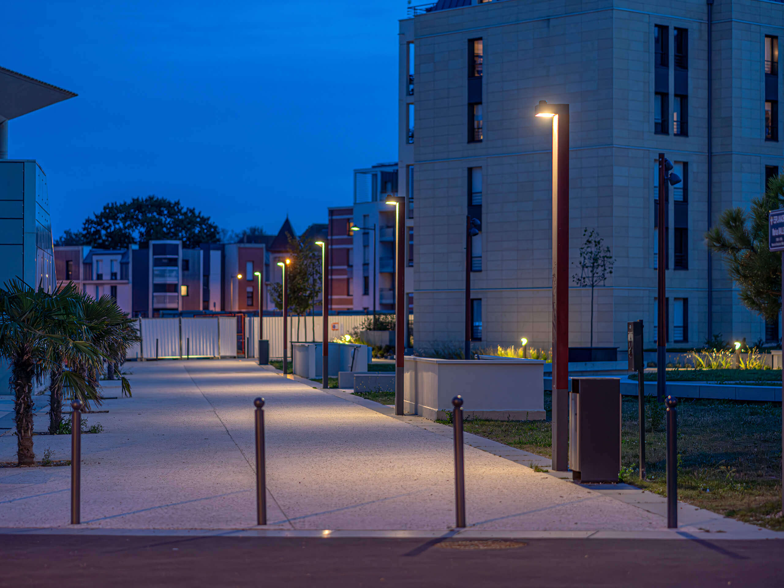 Beleuchteter Fußweg mit modernen Laternen und Stadtmobiliar bei Dämmerung.