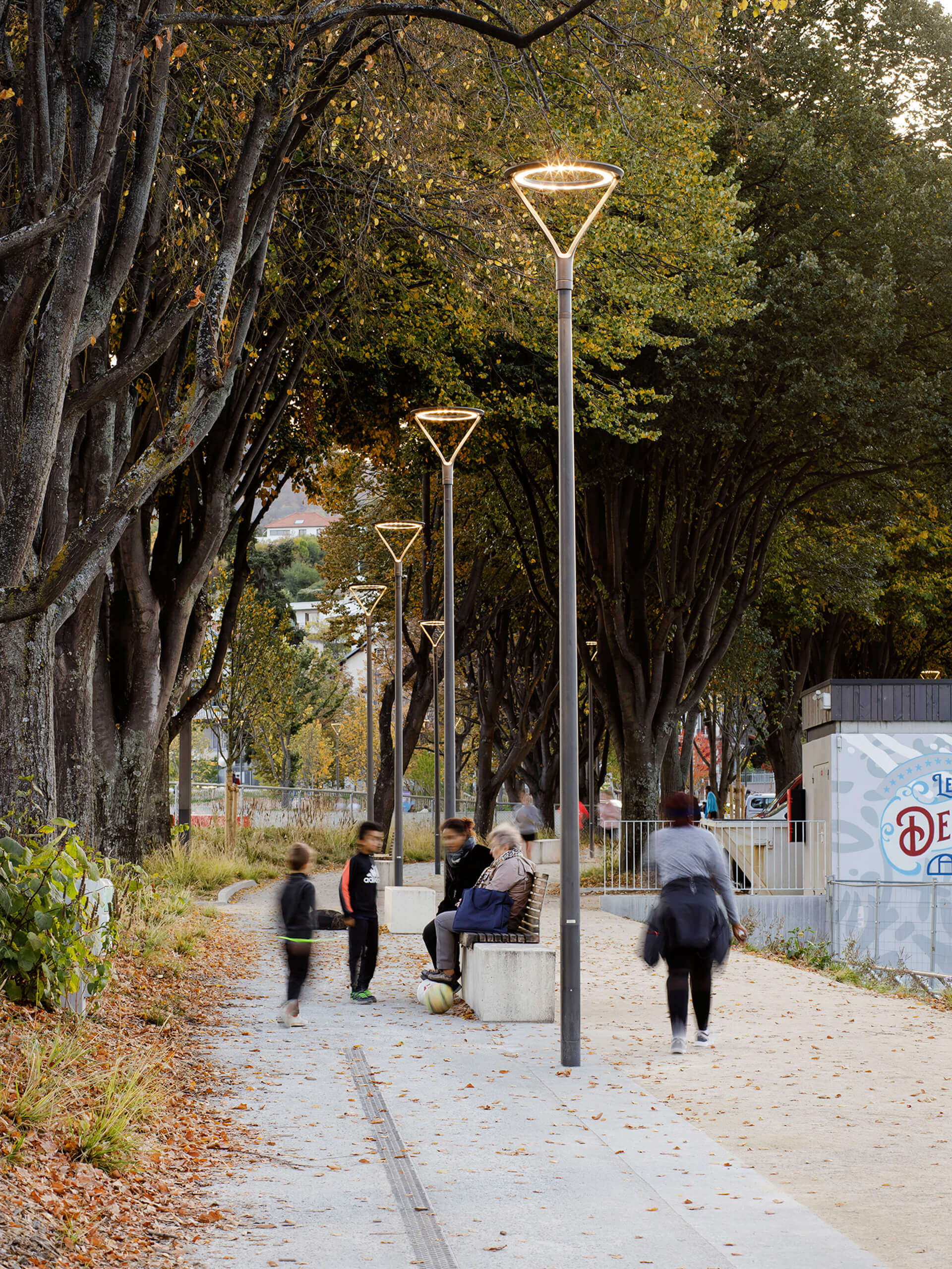 Beleuchteter Parkweg mit Sitzbänken und Spaziergängern, Stadtmobiliar von Illumina