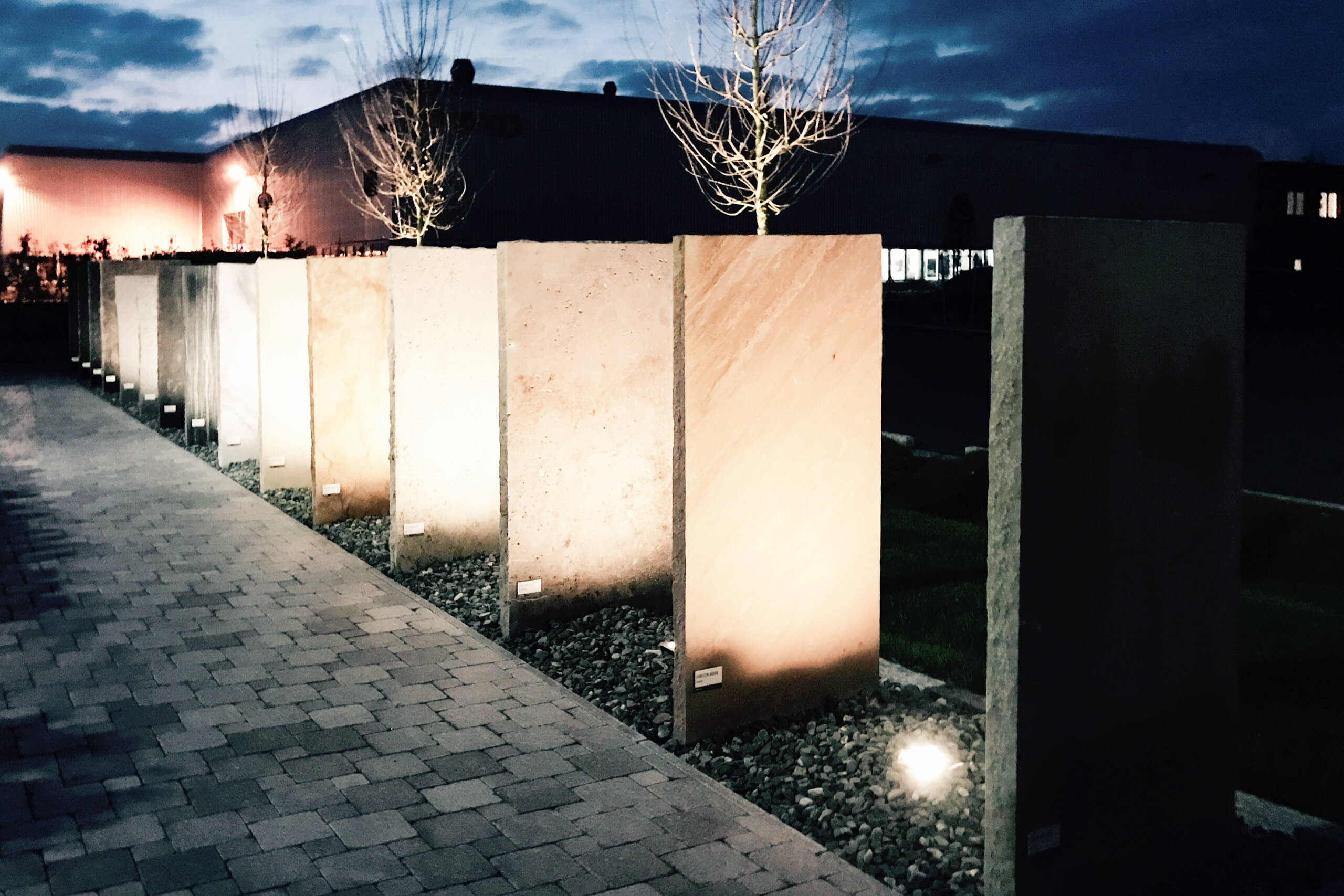 Beleuchtete Betonsäulen mit Bäumen auf einem Gehweg bei Nacht