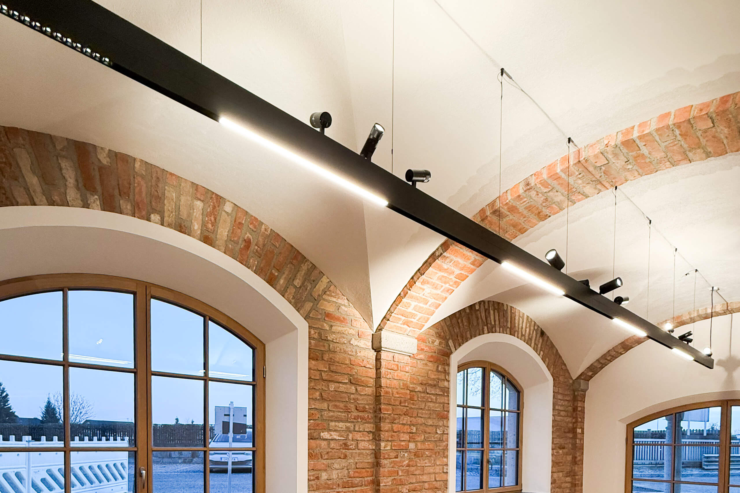 Moderne Lichtplanung von Illumina mit Hängeleuchten über Ziegelbögen und Fenstern.
