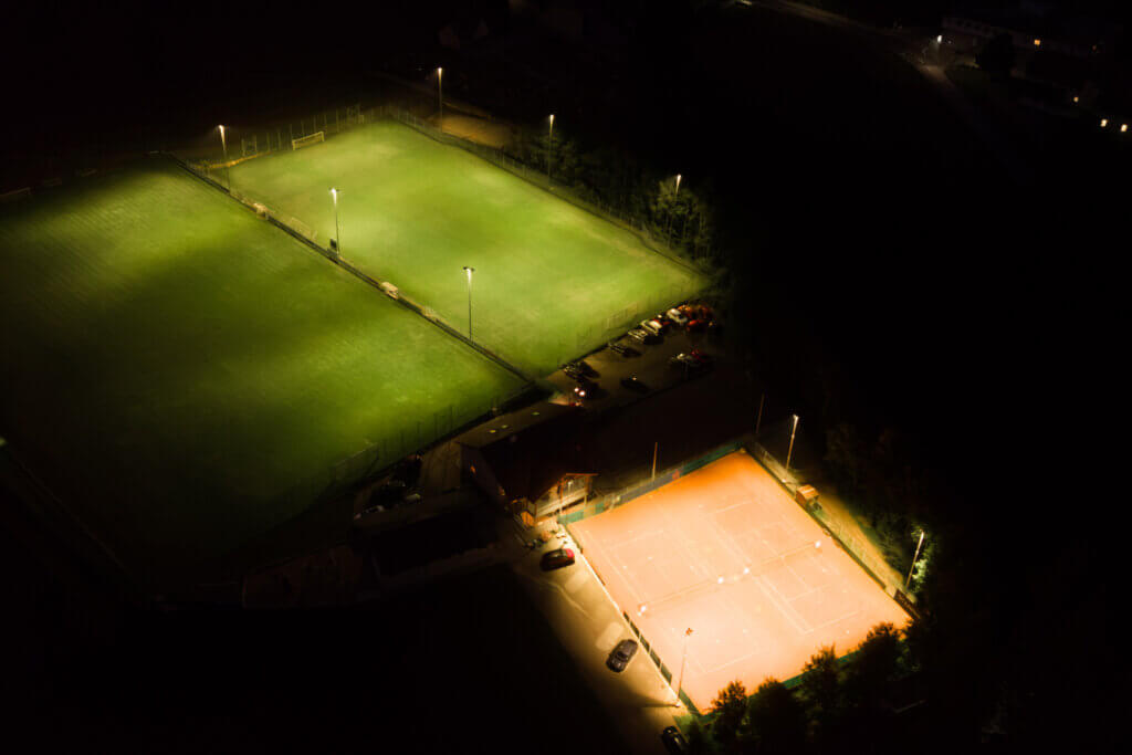 Beleuchtete Sportplätze bei Nacht: Fußballfelder und Tennisplatz mit heller, moderner Beleuchtung.