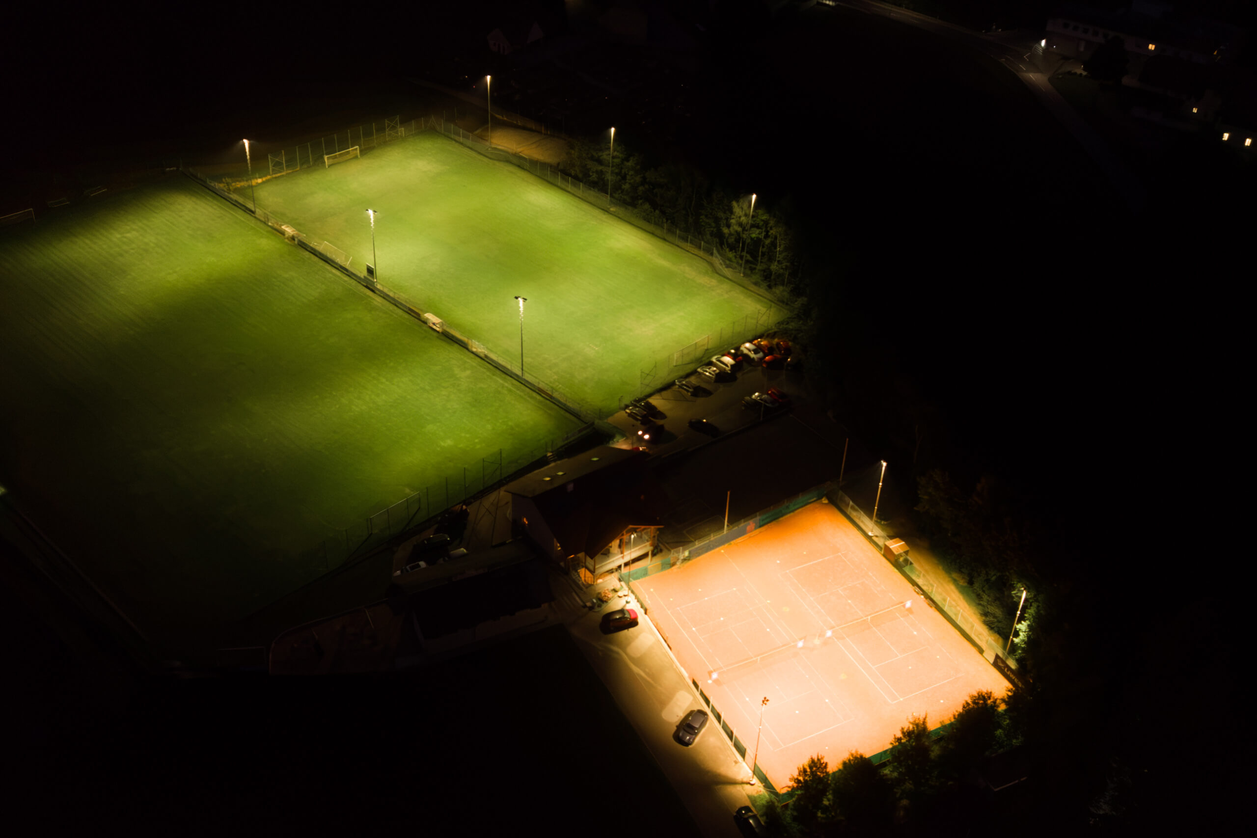 Beleuchtete Sportplätze bei Nacht: Fußballfelder und Tennisplatz mit heller, moderner Beleuchtung.