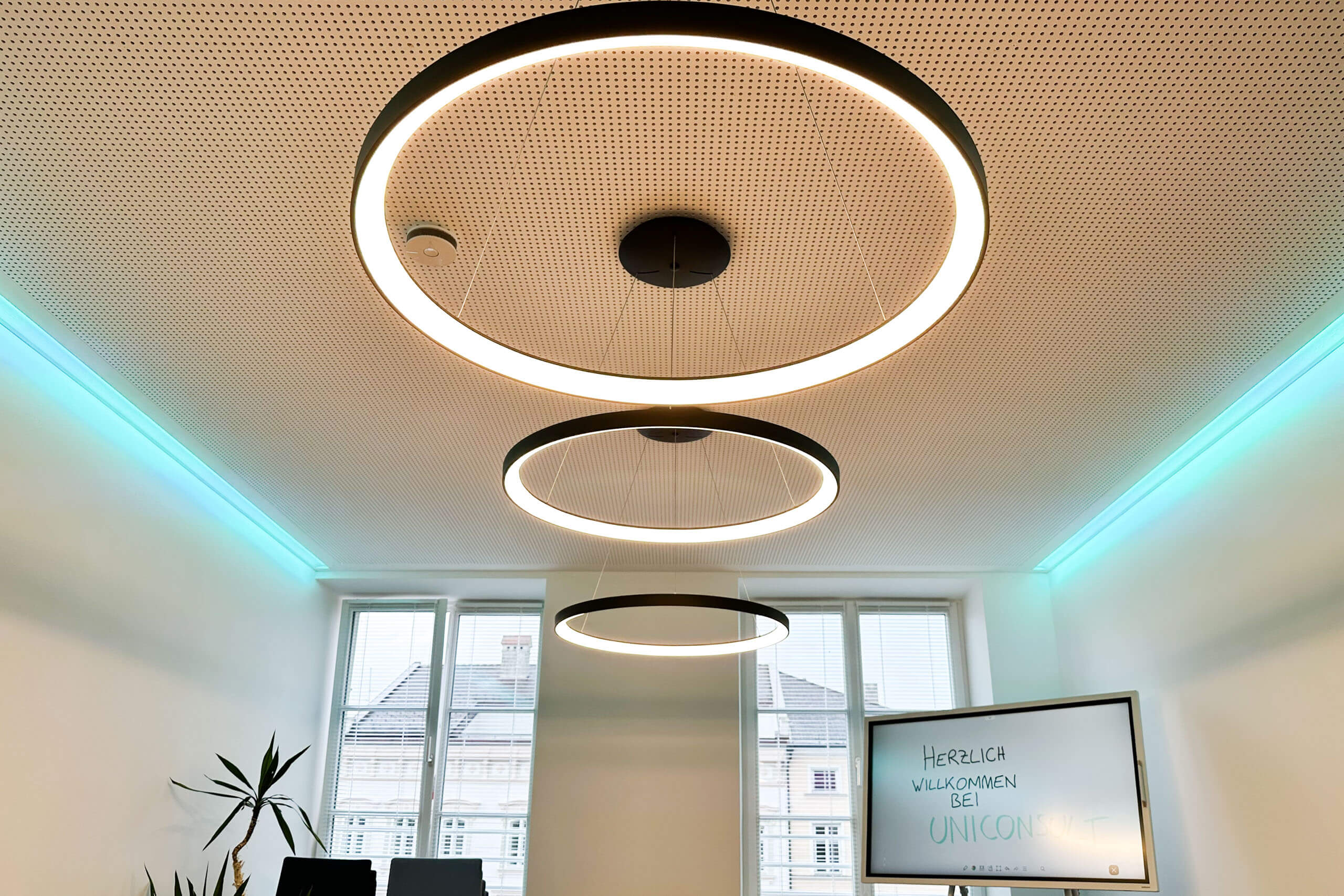 Konferenzraum mit moderner Ring-Pendelleuchten-Beleuchtung und Willkommensgruß auf Bildschirm