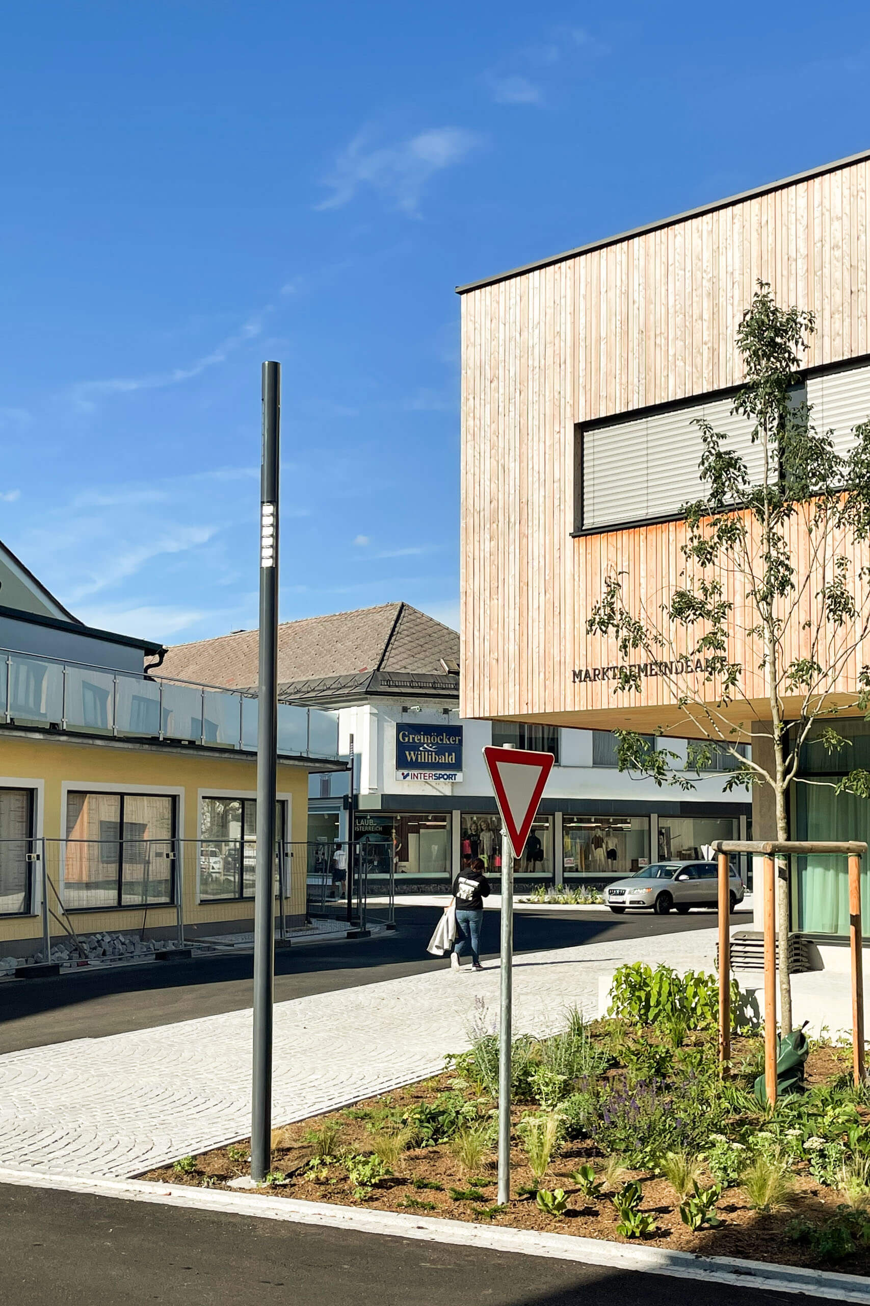 Moderne Holzfassade mit Marktgemeinde-Schild, beleuchtet durch Straßenlaterne.