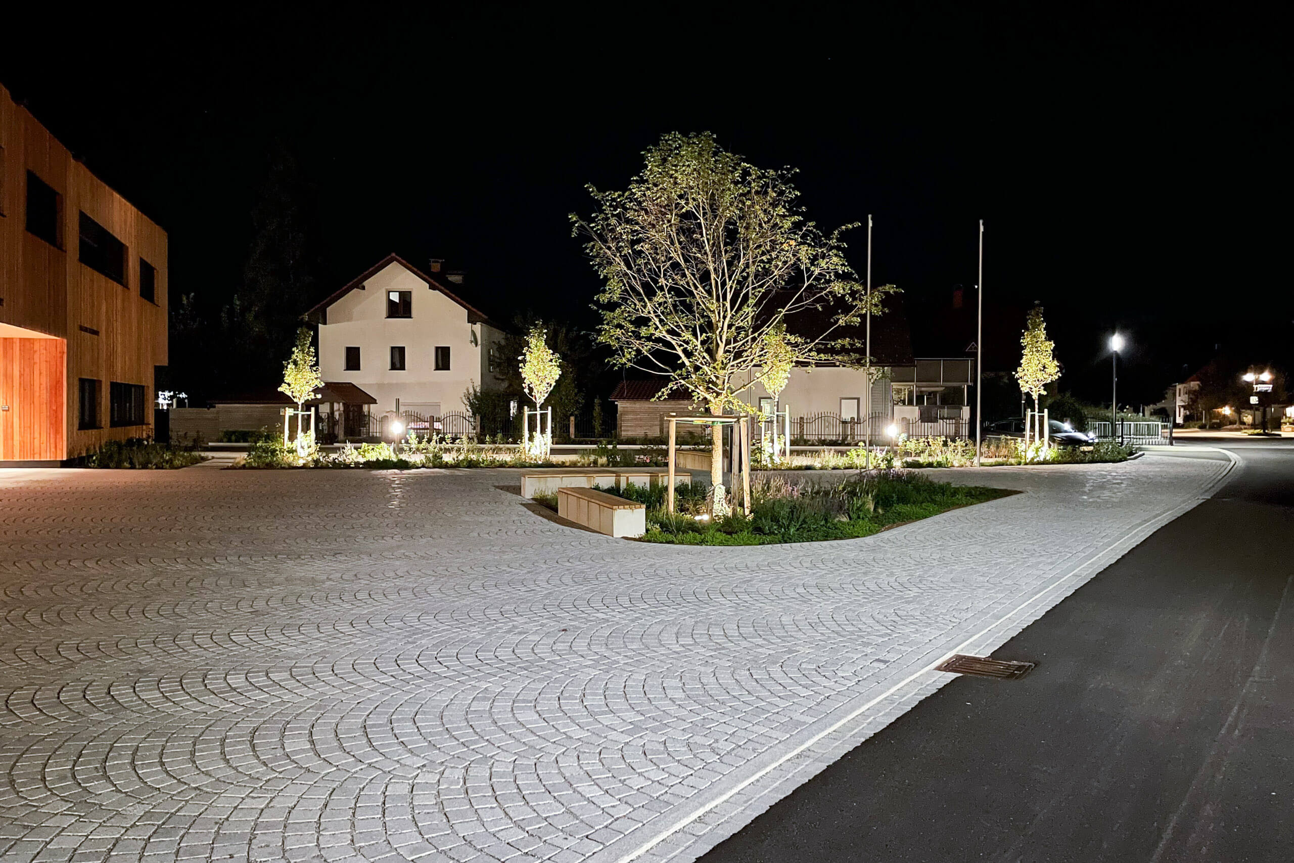 Beleuchteter Platz mit modernen Gebäuden und Bäumen bei Nacht