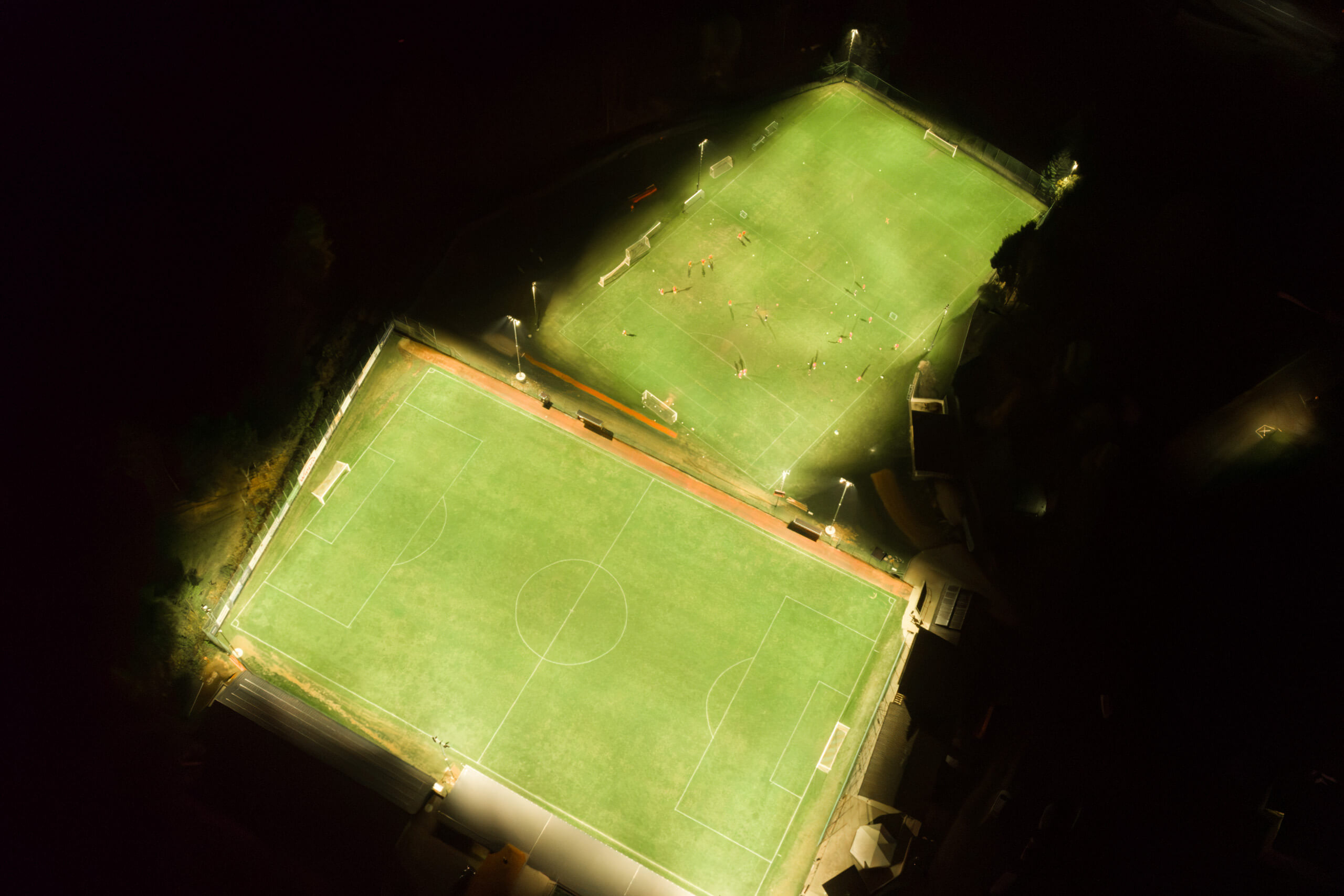 Zwei beleuchtete Fußballfelder bei Nacht, von oben gesehen, mit Spielfeldern und Toren.