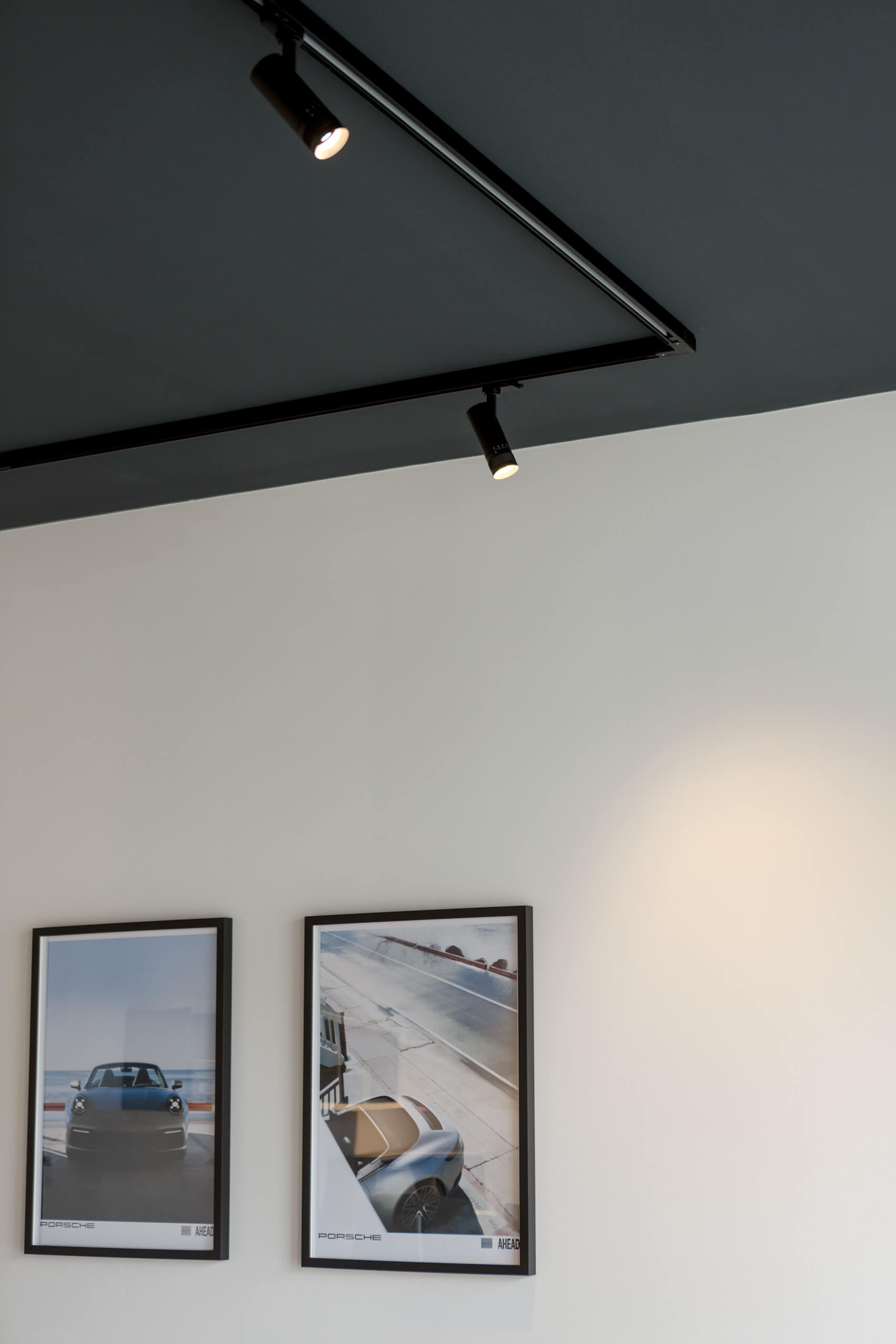 Moderne Lichtschienen mit Strahlern an dunkler Decke über Porsche-Bildern.