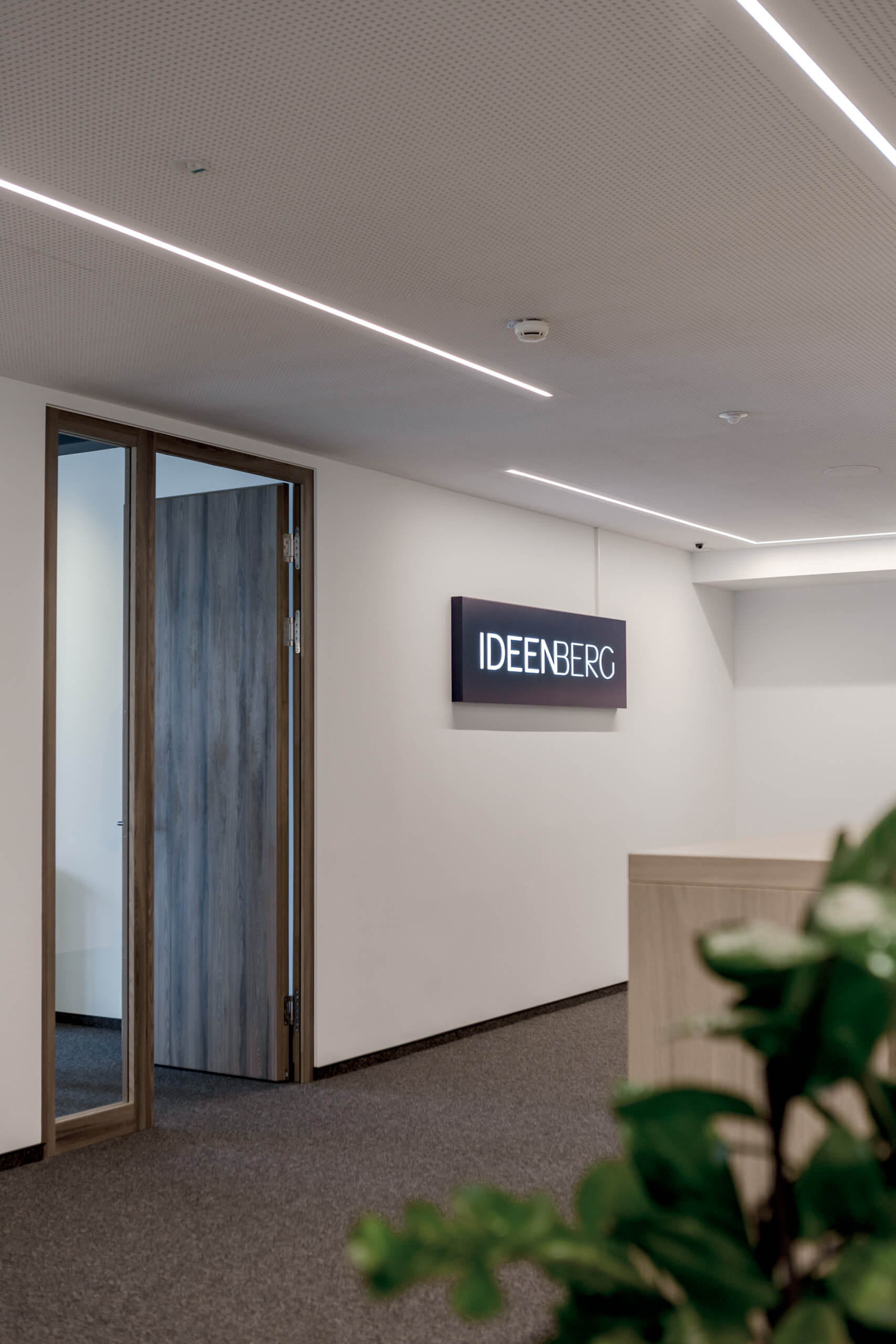 Büroflur mit beleuchtetem "IDEENBERG"-Schild und Holztüren